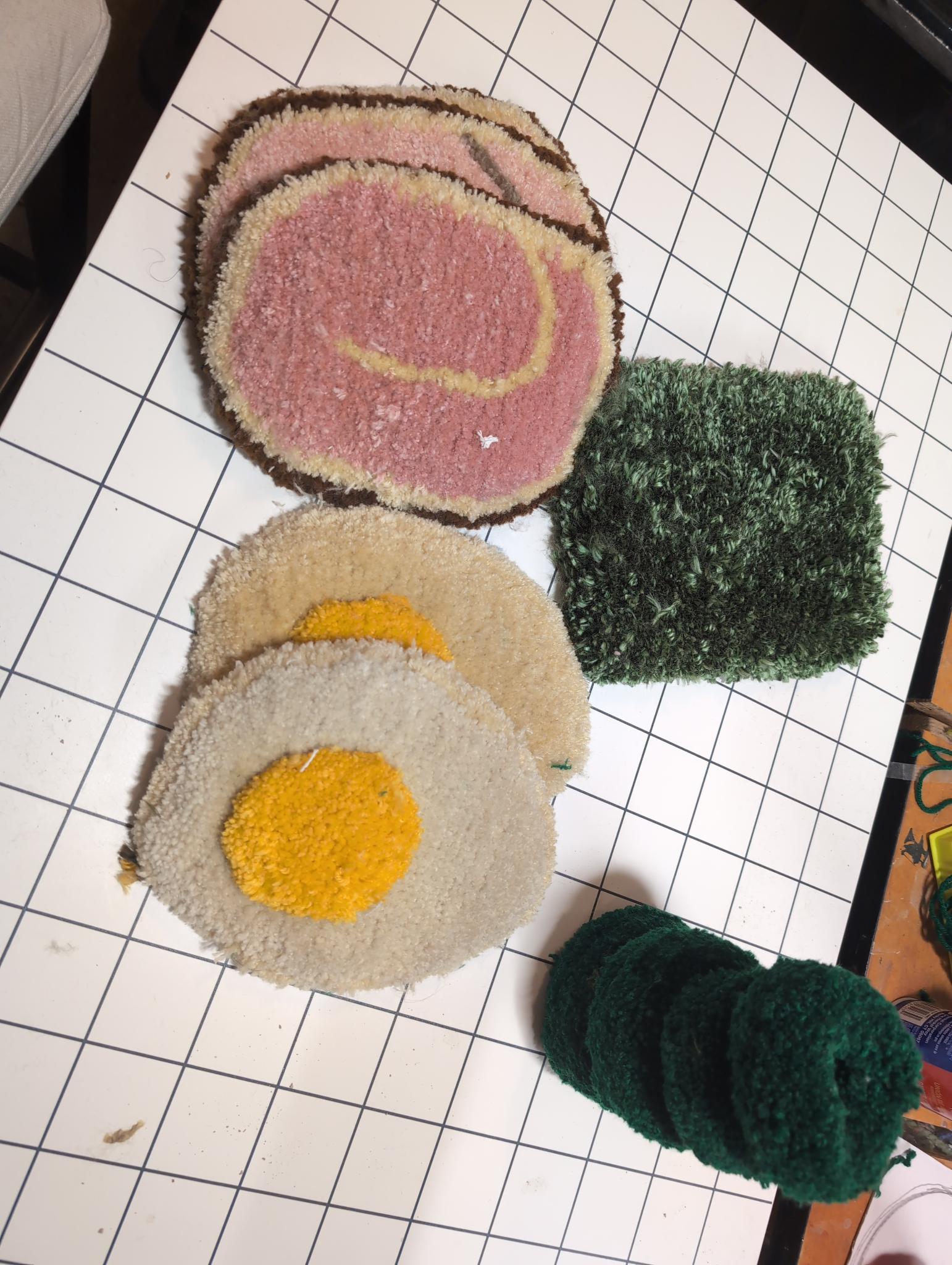 Finished ingredients cut out and laid on a gridded cutting mat: chashu slices, two egg halves, a shaggy green nori square, and folded green onion rings