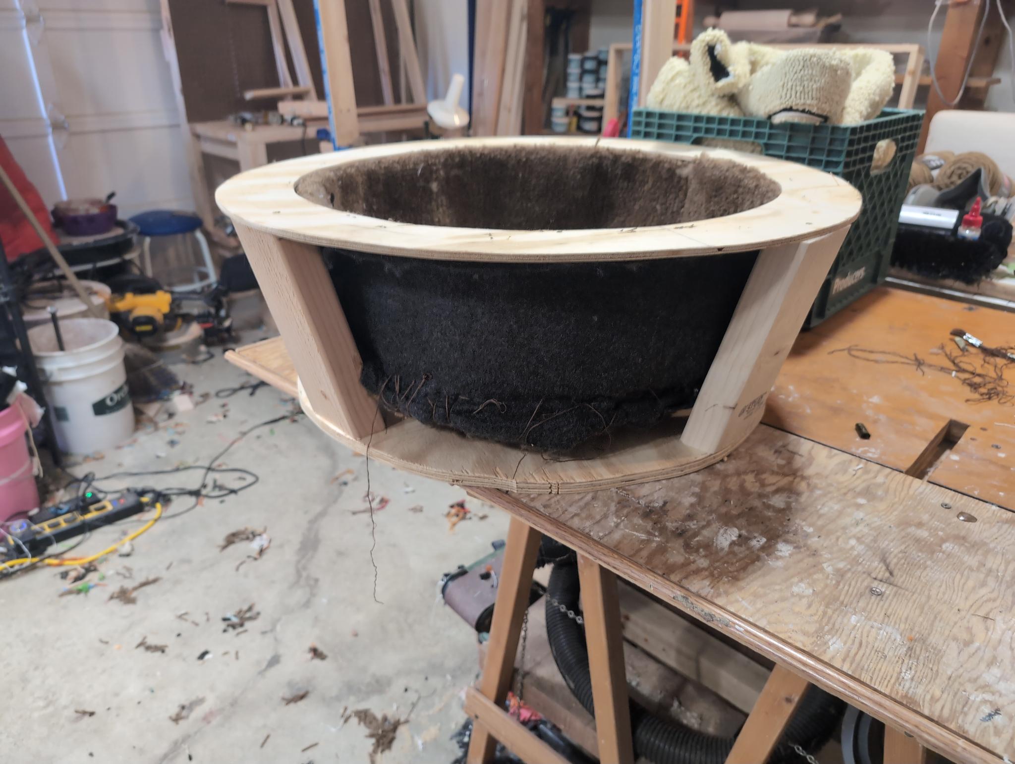 The bare plywood bowl skeleton on a sawhorse: a plywood ring on vertical posts, black tufted lining inside